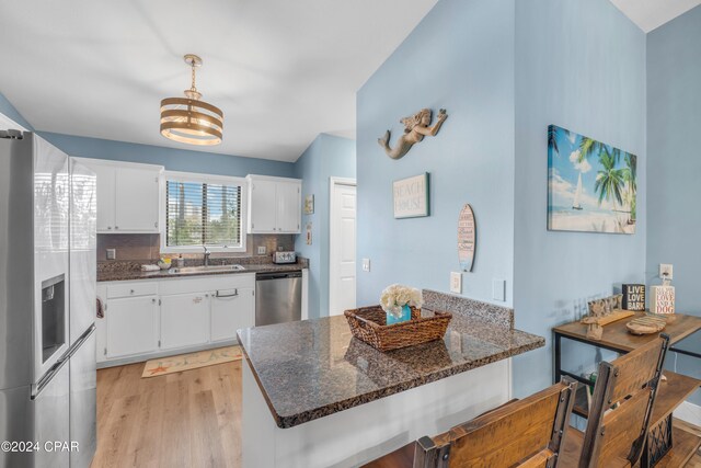 kitchen with decorative backsplash, stainless steel appliances, sink, white cabinets, and light hardwood / wood-style floors