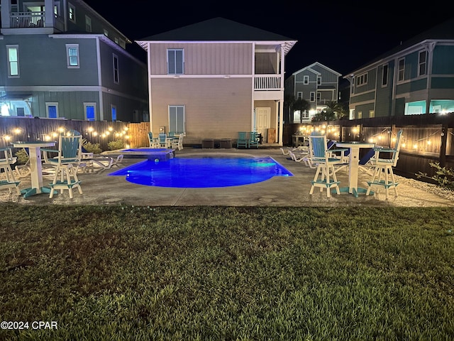 pool at night featuring a lawn and a patio area