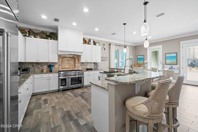 kitchen featuring light stone countertops, decorative light fixtures, high quality appliances, a center island with sink, and white cabinets