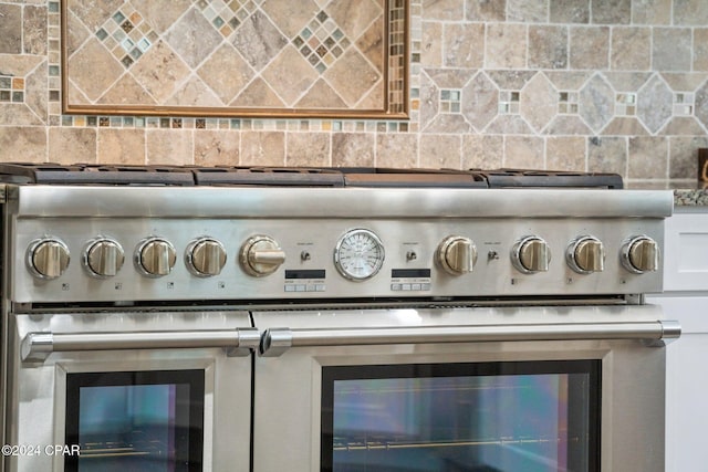 interior details featuring backsplash, high end stainless steel range, and white cabinets