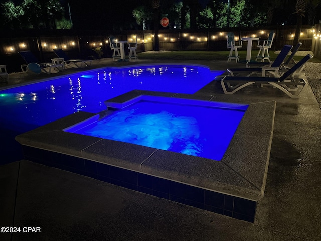 pool at twilight featuring an in ground hot tub and a patio