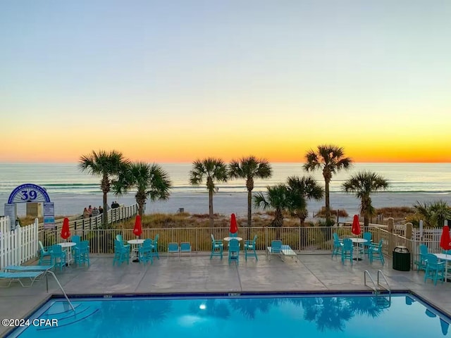 pool at dusk with a water view and a patio area