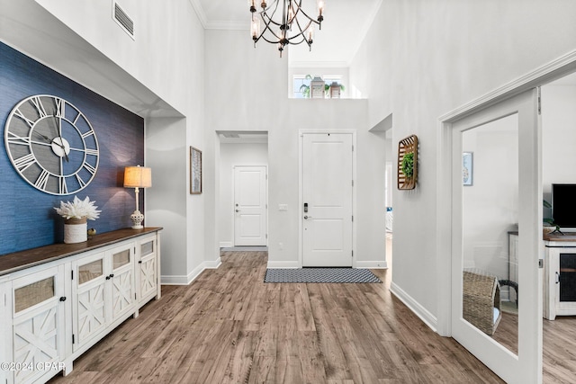 entryway with a chandelier, hardwood / wood-style floors, crown molding, and a high ceiling