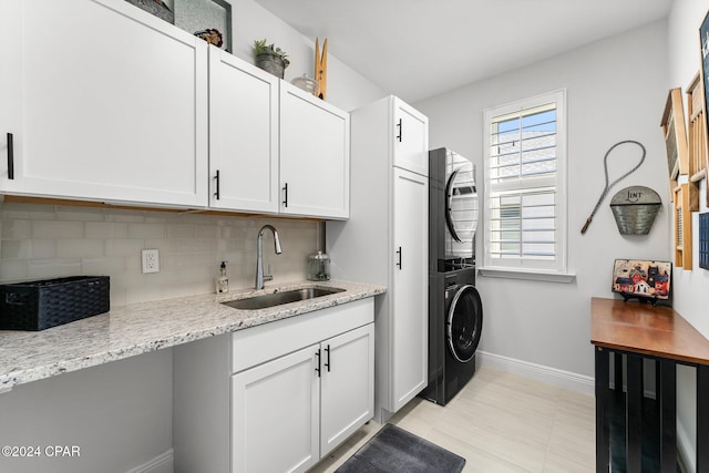 laundry room featuring cabinets, stacked washing maching and dryer, and sink