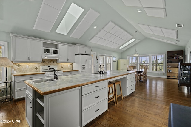 kitchen with white appliances, dark wood-type flooring, lofted ceiling with skylight, white cabinets, and an island with sink