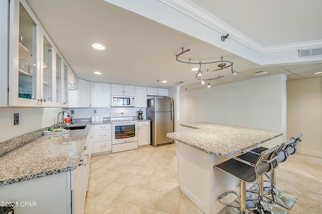 kitchen with crown molding, a breakfast bar area, visible vents, a sink, and white appliances