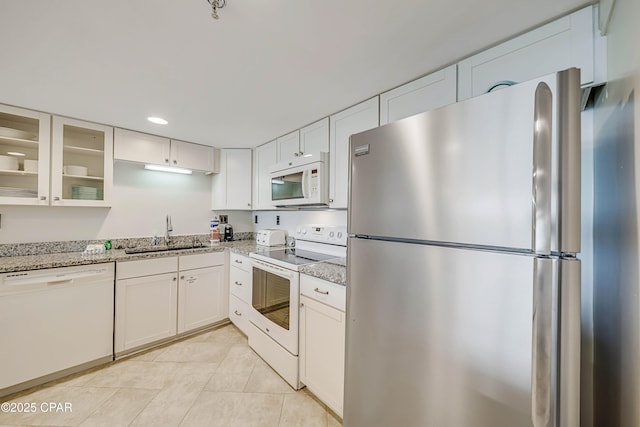 kitchen featuring white appliances, light tile patterned floors, light stone counters, white cabinetry, and a sink