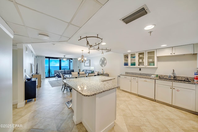 kitchen with visible vents, a kitchen island, light stone counters, white dishwasher, and a sink