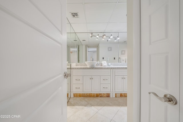 full bath with tile patterned flooring, a paneled ceiling, a sink, visible vents, and double vanity