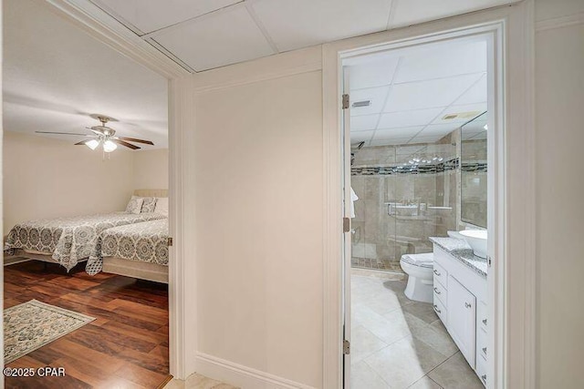 bedroom featuring a ceiling fan, a paneled ceiling, light wood finished floors, and ensuite bathroom