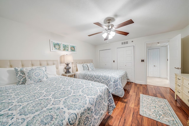 bedroom with two closets, visible vents, ceiling fan, wood finished floors, and baseboards