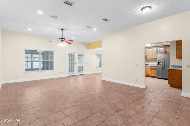 unfurnished living room featuring ceiling fan, light tile patterned floors, a textured ceiling, and french doors