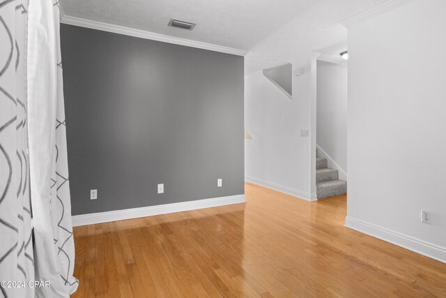 empty room featuring wood-type flooring, a textured ceiling, and ornamental molding