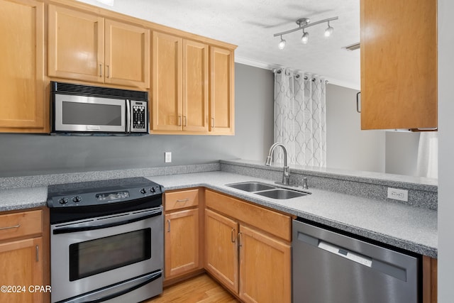 kitchen featuring sink, stainless steel appliances, kitchen peninsula, track lighting, and light wood-type flooring