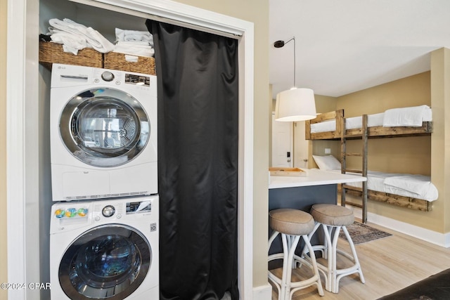 clothes washing area featuring wood-type flooring and stacked washer / dryer