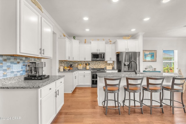 kitchen featuring white cabinetry, stainless steel appliances, light stone counters, crown molding, and a kitchen island with sink