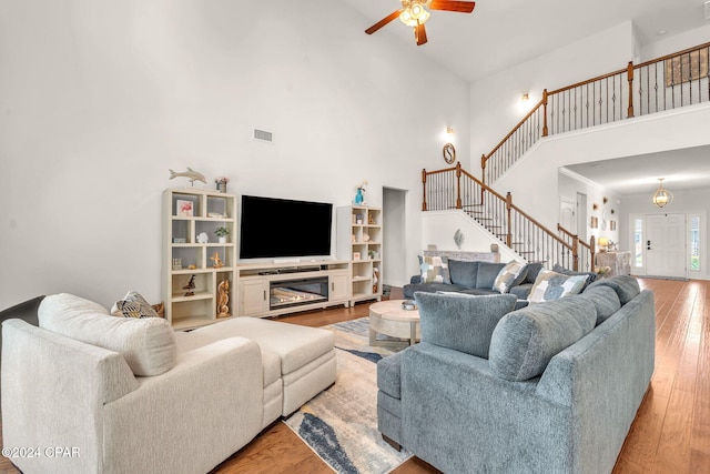 living room with ceiling fan, light wood-type flooring, a towering ceiling, and a fireplace