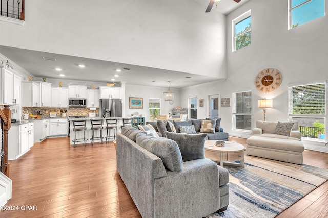 living room featuring ceiling fan, light hardwood / wood-style flooring, crown molding, and a high ceiling