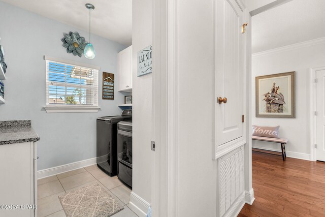 clothes washing area with washer and clothes dryer, cabinets, light tile patterned floors, and crown molding