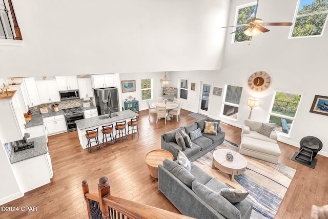 living room featuring ceiling fan, light wood-type flooring, a towering ceiling, and sink