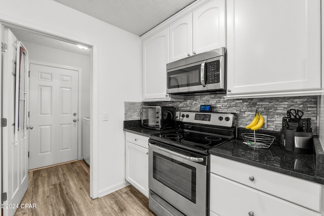 kitchen with appliances with stainless steel finishes, backsplash, white cabinetry, and dark stone countertops