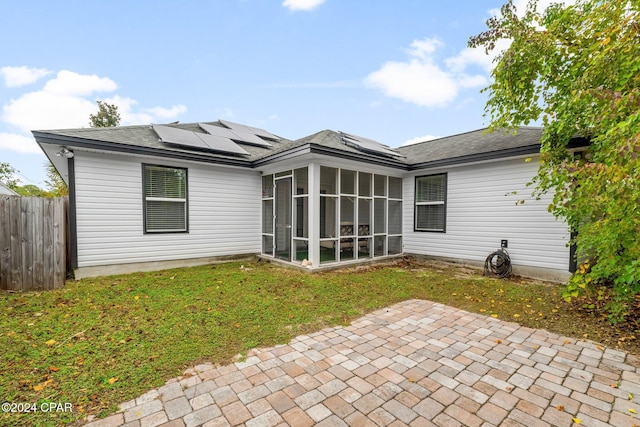 rear view of house with solar panels, a yard, a patio area, and a sunroom