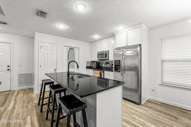 kitchen with sink, dark stone countertops, a breakfast bar, white cabinets, and appliances with stainless steel finishes