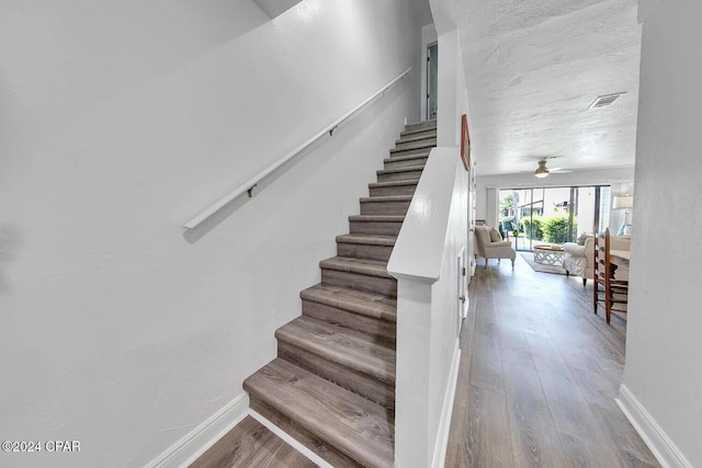 staircase with ceiling fan and hardwood / wood-style floors