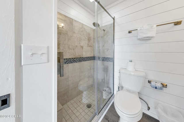 bathroom featuring hardwood / wood-style floors, toilet, a shower with shower door, and wood walls