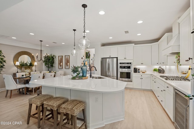 kitchen featuring stainless steel appliances, beverage cooler, a center island with sink, white cabinets, and light hardwood / wood-style floors