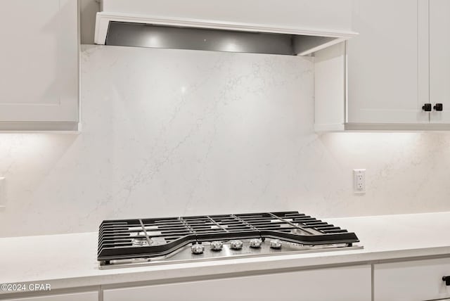 details featuring white cabinets, stainless steel gas stovetop, and wall chimney range hood