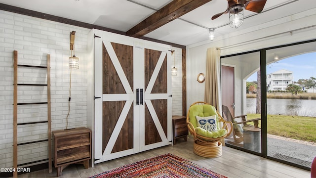 interior space with a water view, hardwood / wood-style flooring, ceiling fan, a barn door, and beam ceiling