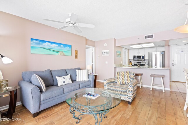 living room with ceiling fan, sink, a textured ceiling, and light wood-type flooring