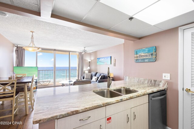 kitchen featuring sink, ceiling fan, light stone countertops, expansive windows, and stainless steel dishwasher