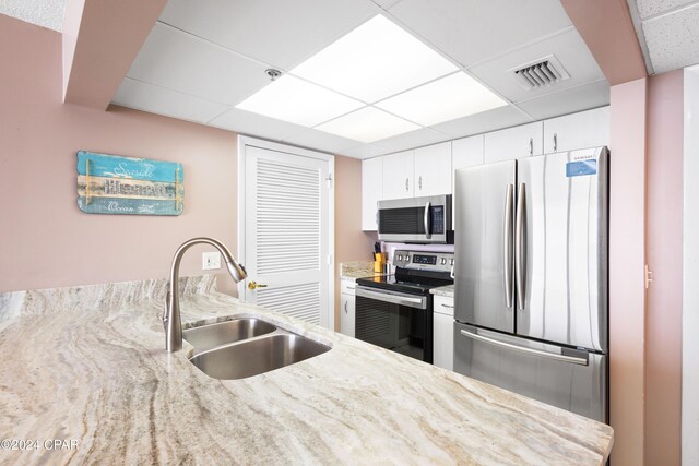 kitchen with sink, light stone counters, a paneled ceiling, appliances with stainless steel finishes, and white cabinets