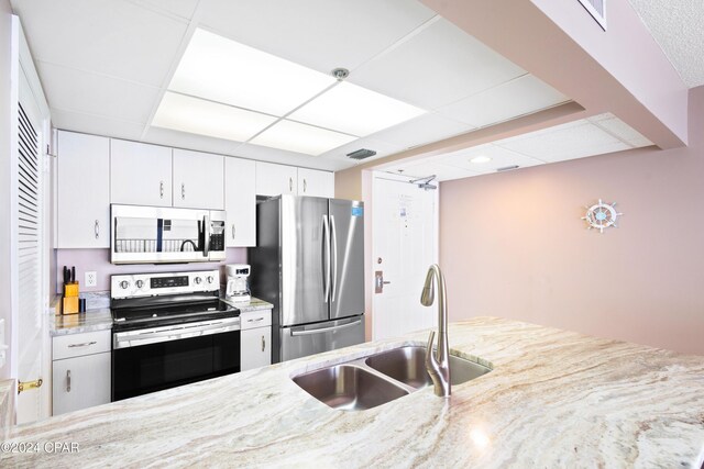 kitchen featuring a paneled ceiling, white cabinetry, sink, stainless steel appliances, and light stone countertops