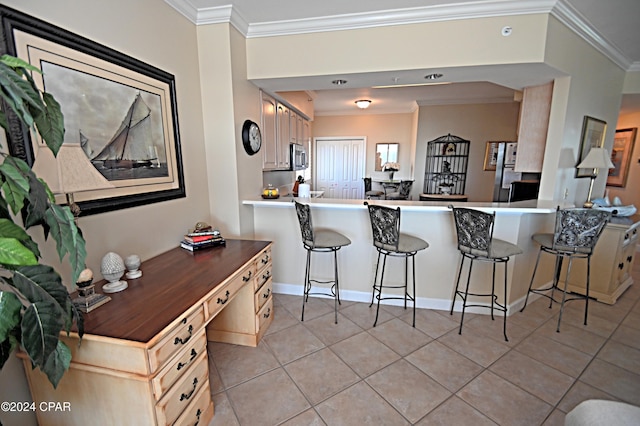 kitchen with a peninsula, a kitchen bar, appliances with stainless steel finishes, and ornamental molding