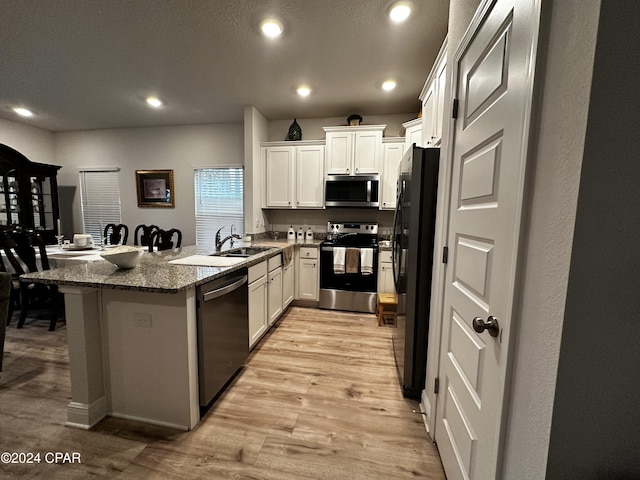 kitchen with sink, white cabinets, dark stone counters, kitchen peninsula, and stainless steel appliances