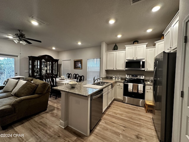 kitchen with appliances with stainless steel finishes, light hardwood / wood-style flooring, white cabinets, and kitchen peninsula