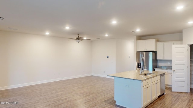 kitchen with white cabinets, stainless steel appliances, light stone counters, and a kitchen island with sink