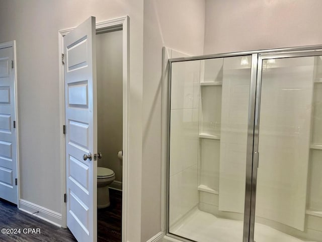 bathroom with hardwood / wood-style flooring, toilet, and a shower with door