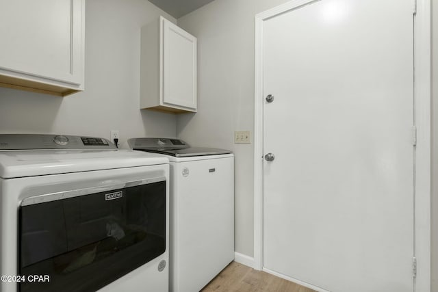 washroom with washing machine and clothes dryer, light hardwood / wood-style flooring, and cabinets