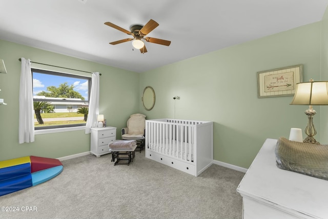 bedroom featuring light carpet, a nursery area, and ceiling fan