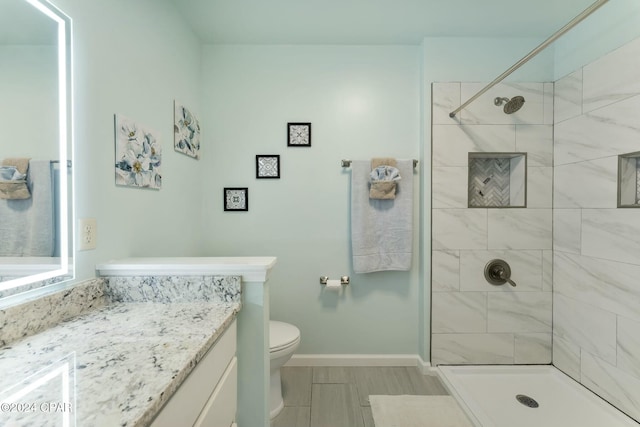 bathroom with a tile shower, vanity, and toilet