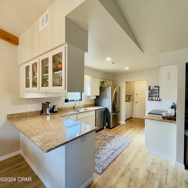 kitchen with kitchen peninsula, appliances with stainless steel finishes, sink, independent washer and dryer, and white cabinetry