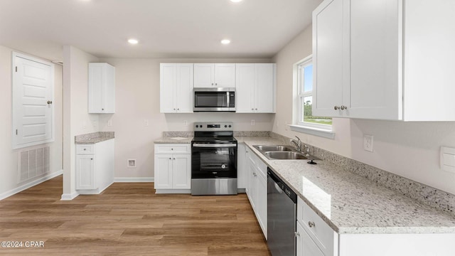 kitchen featuring white cabinetry, stainless steel appliances, light wood-type flooring, light stone countertops, and sink