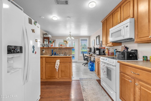 kitchen with sink, dark wood-type flooring, hanging light fixtures, a notable chandelier, and white appliances