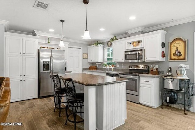 kitchen featuring a center island, crown molding, white cabinetry, a breakfast bar, and stainless steel appliances