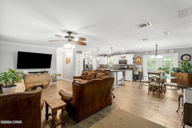 living room featuring ceiling fan with notable chandelier, ornamental molding, and a textured ceiling