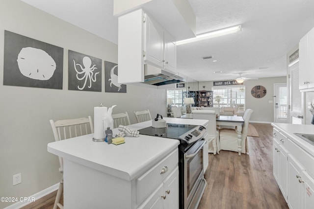 kitchen featuring hardwood / wood-style floors, a center island, a kitchen breakfast bar, stainless steel electric range oven, and white cabinetry